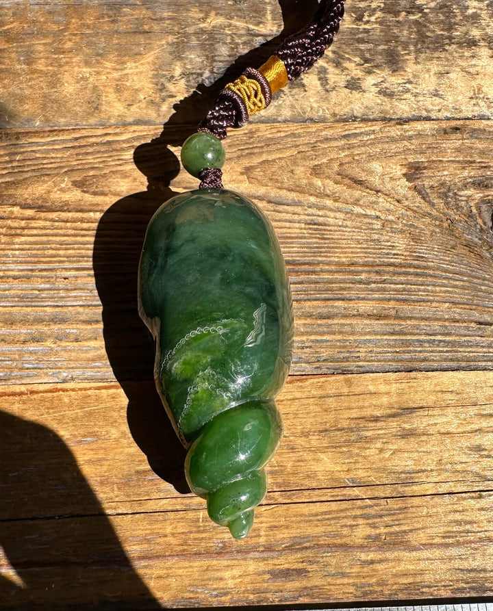 Top view of the green shell shaped pendant with a round bead on a braided cord against wood