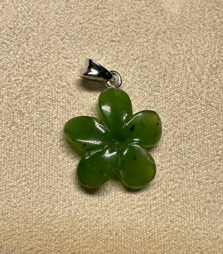 Green jade flower pendant with a silver bail against a textured beige background.