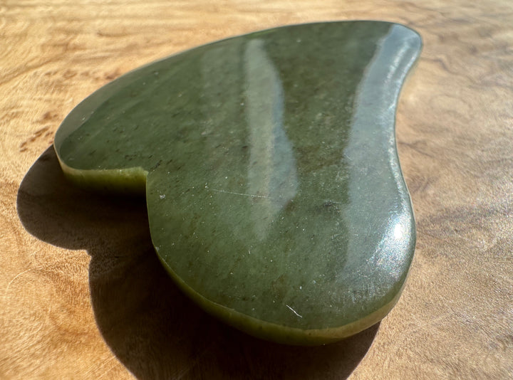 Close-up of low grade nephrite jade gua sha tool edge on brown fabric