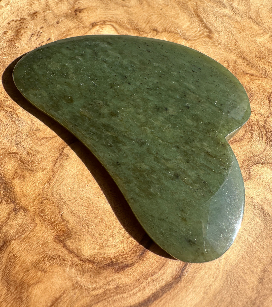 Low grade nephrite jade gua sha tool resting on textured brown fabric