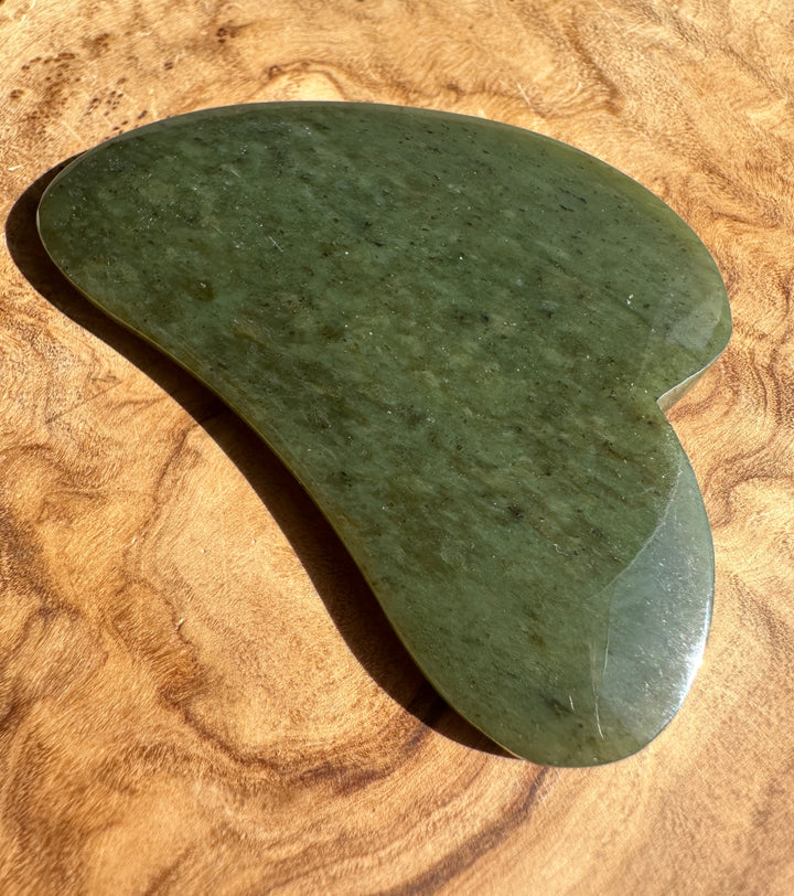 Low grade nephrite jade gua sha tool resting on textured brown fabric