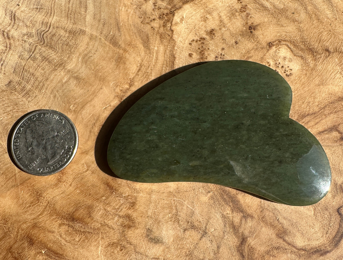 Low grade nephrite jade gua sha tool with a coin for scale on textured brown fabric