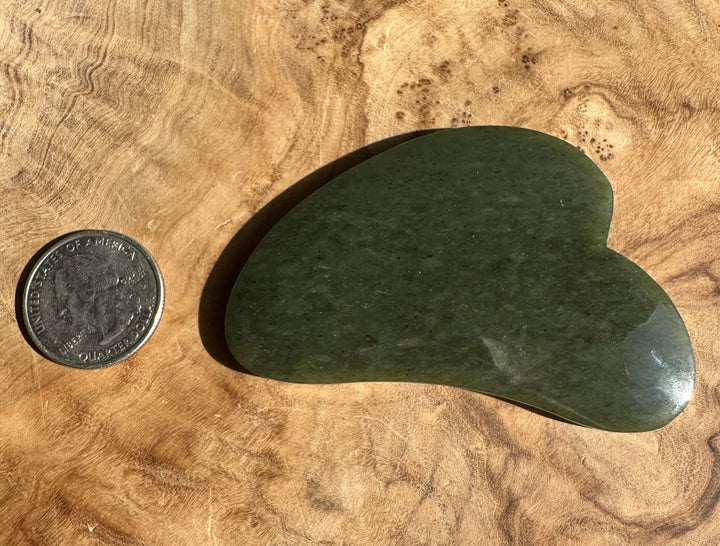 Low grade nephrite jade gua sha tool with a coin for scale on textured brown fabric