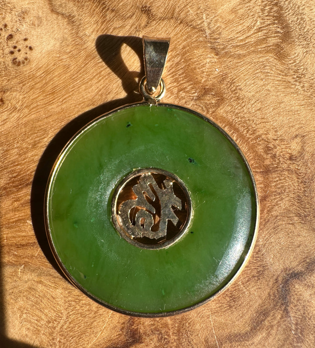 Angled view of the green nephrite jade Fu Pi disc pendant with carved central motif visible.