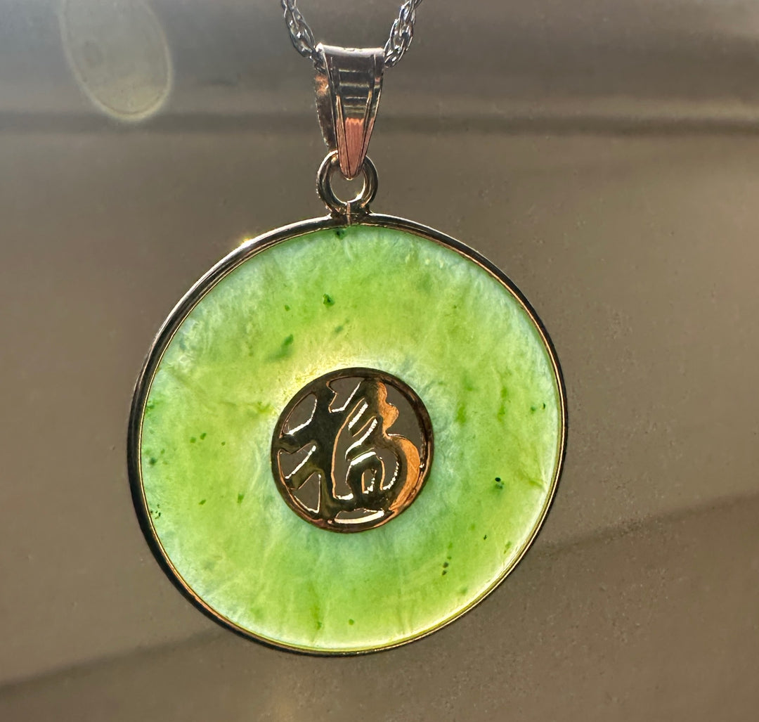 Green nephrite jade disc pendant with silver bezel and a circular black medallion with gold markings.