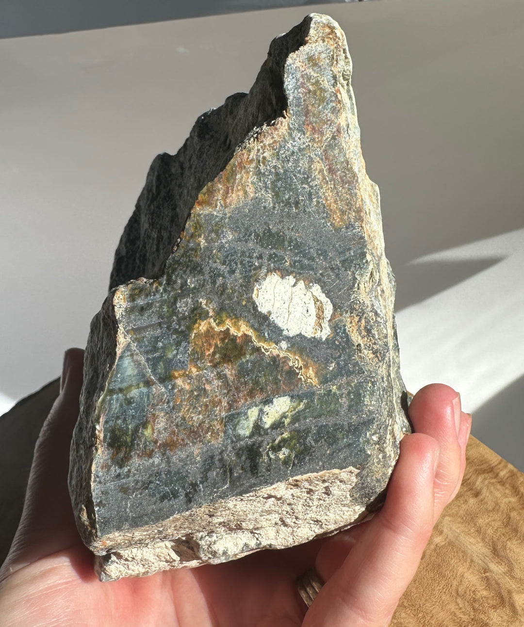 Side view of Wyoming Black Jade showing multicolored veining and rough texture, held in hand.