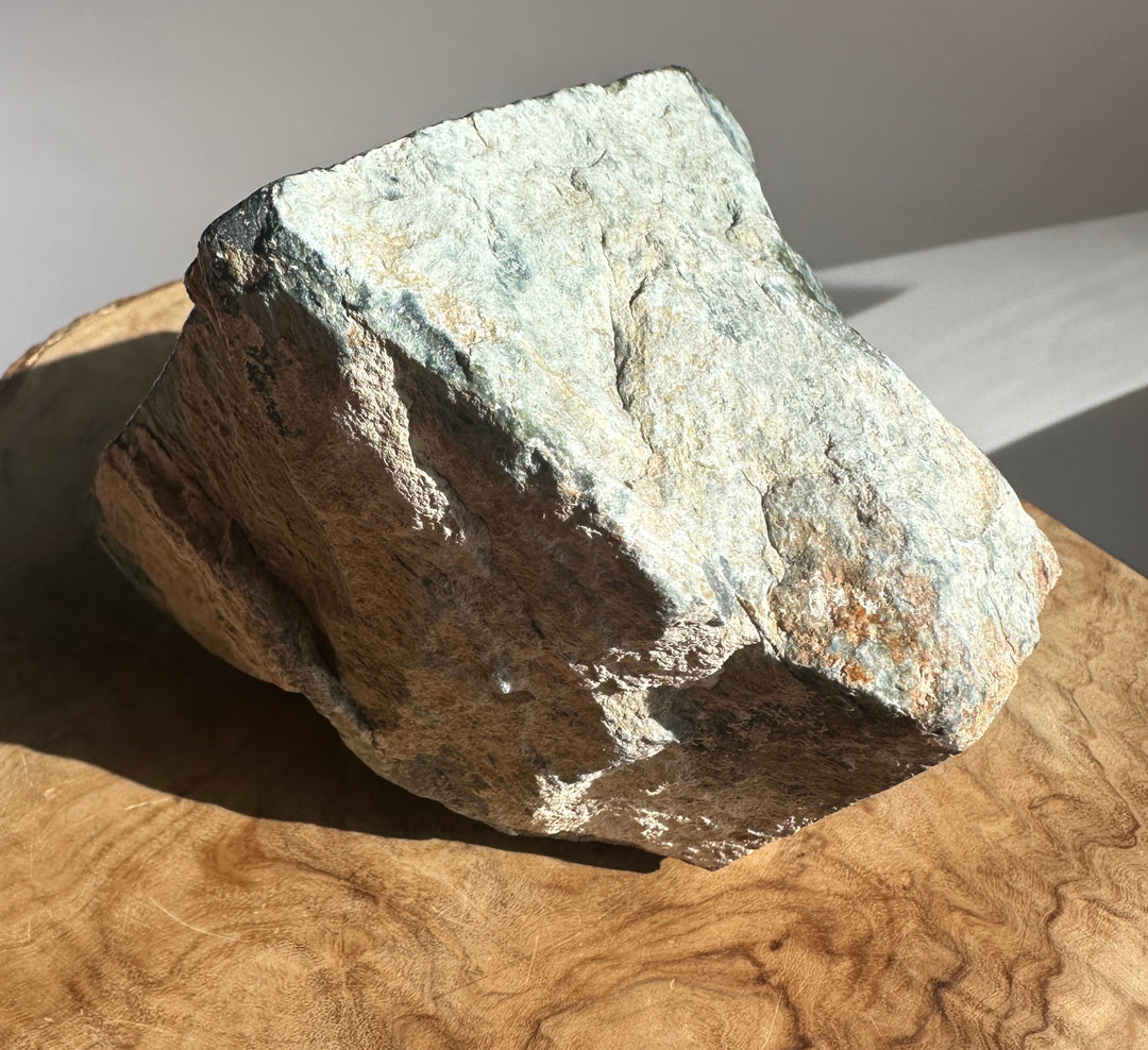 Rough Wyoming Black Jade chunk with gray and tan tones resting on a wooden surface.