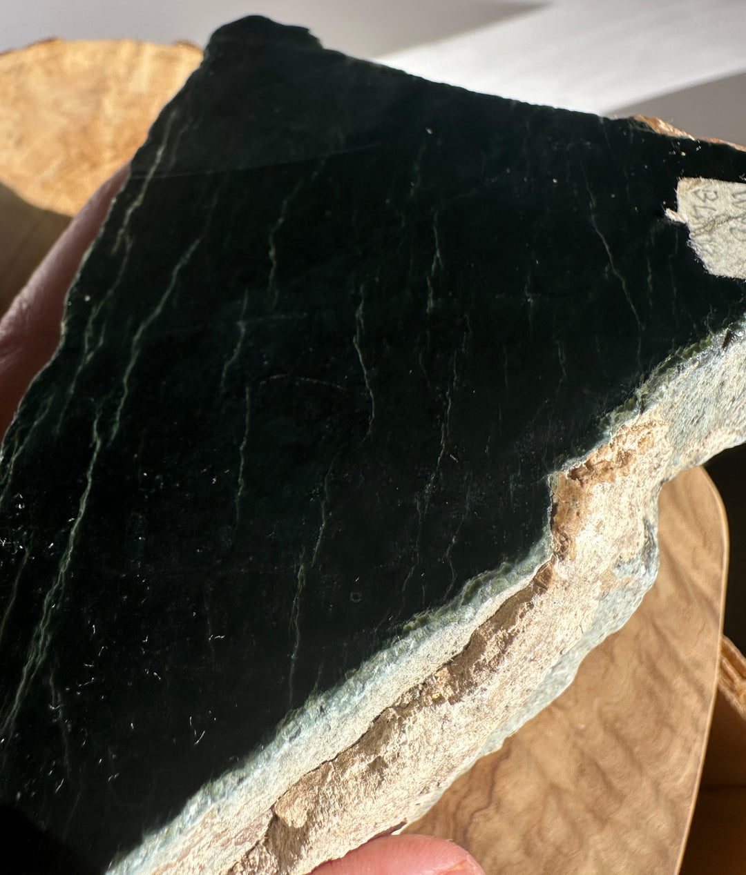 Close up of black jade showing dark surface with white veining on a rough rock placed on wood.