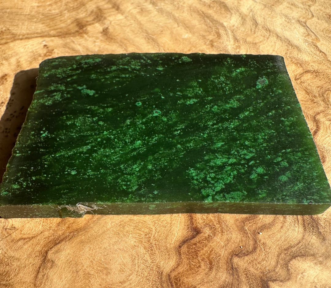 Dark green Cassiar jade slab with mottled lighter green patches on a wooden surface.