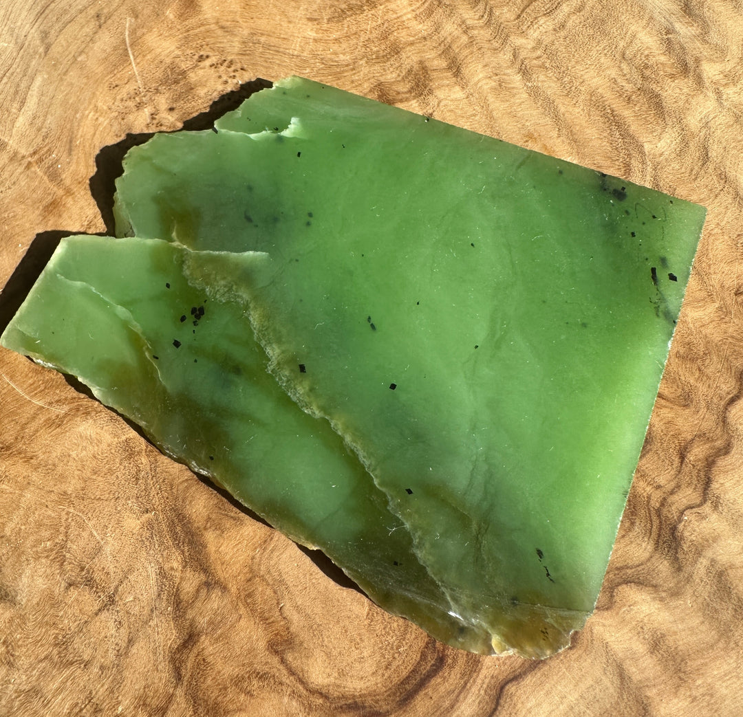 Apple green nephrite jade slab with a jagged edge on a wooden surface