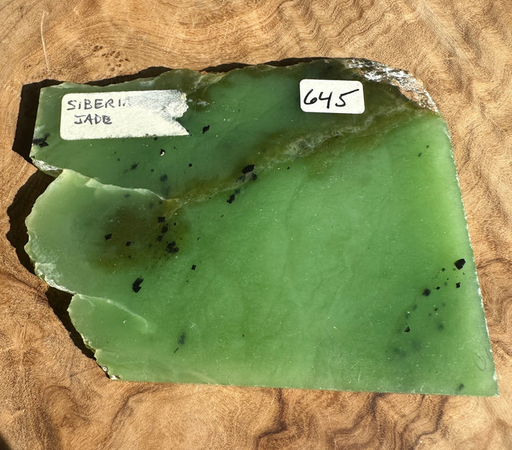 Apple green nephrite jade slab with a white label on a wooden surface.