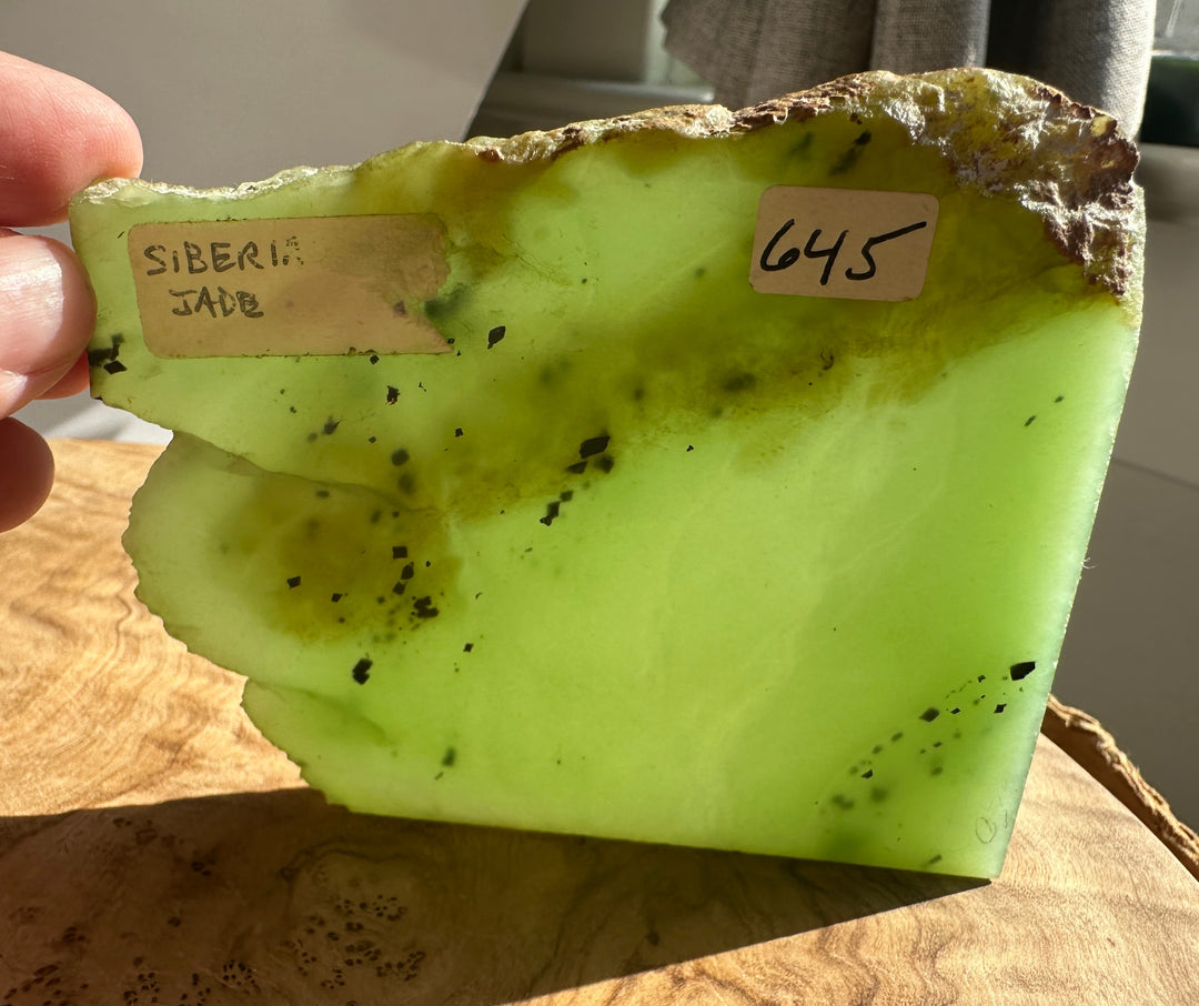 Apple green nephrite jade slab held in hand with a white label on its surface.