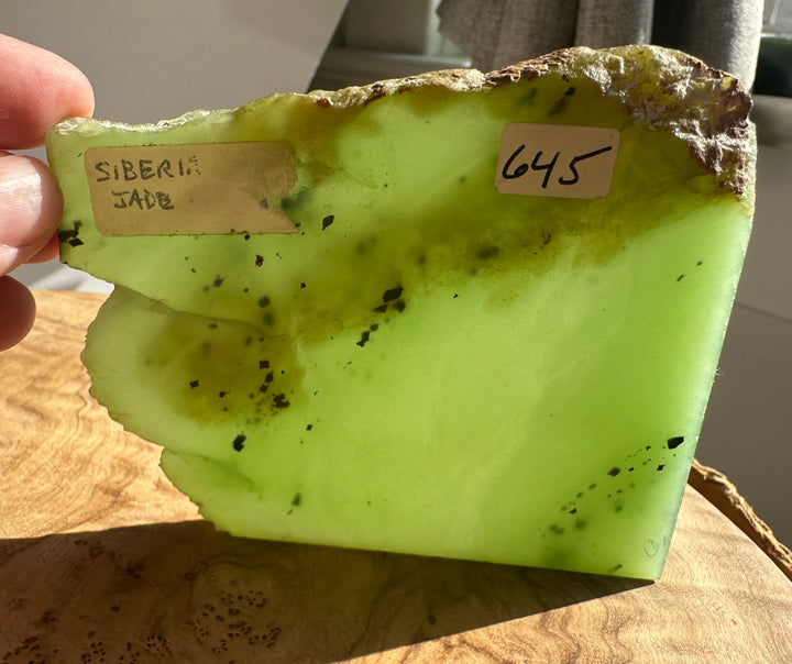 Apple green nephrite jade slab held in hand with a white label on its surface.