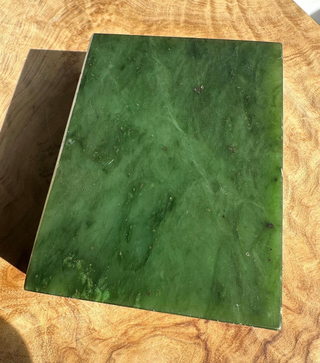 Rectangular block of rough Canadian jade in dark green on a wooden table