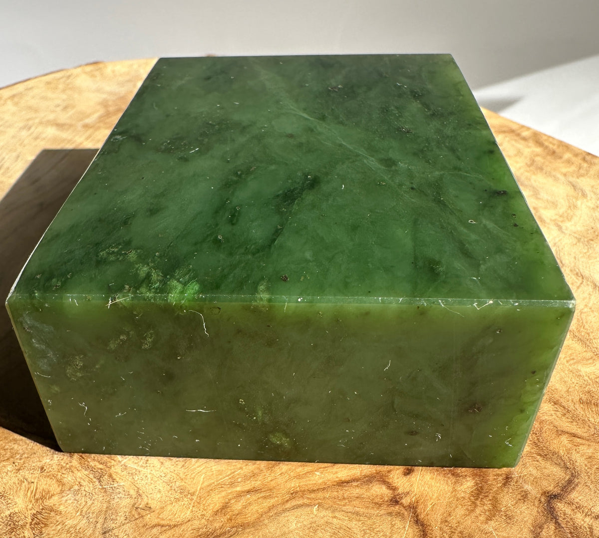 Canadian Rough Jade block in deep green resting on a light wood surface.