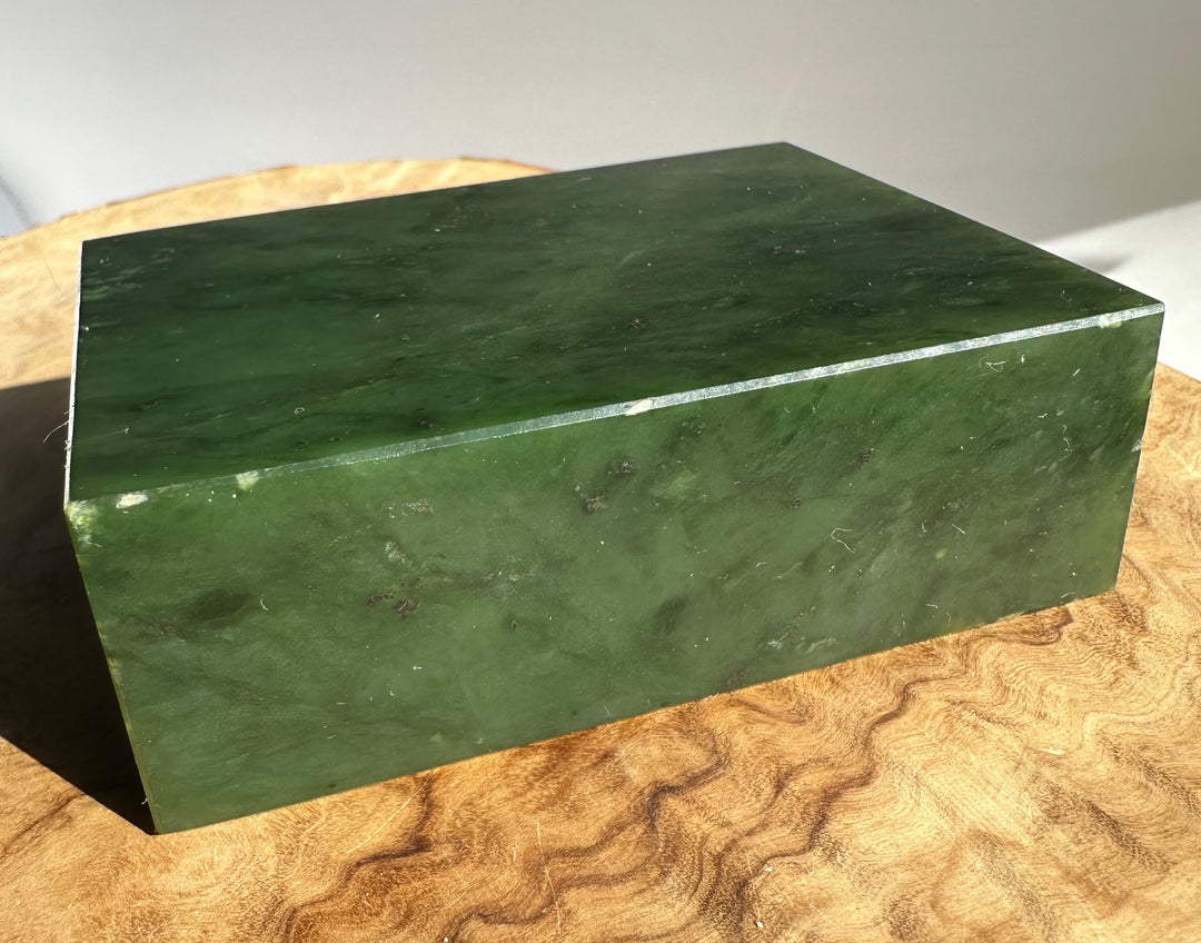 Deep green jade slab viewed from a low angle on a light wooden surface.