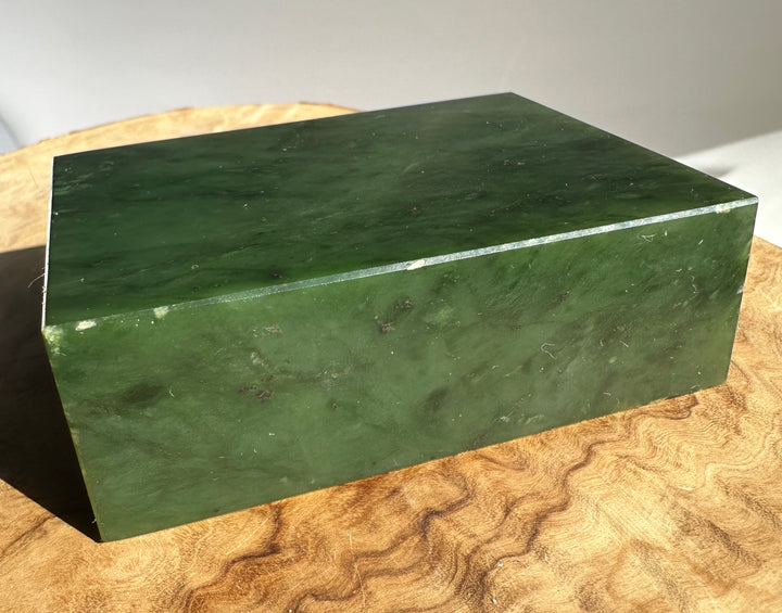 Deep green jade slab viewed from a low angle on a light wooden surface.