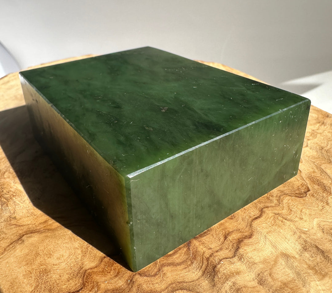 Green jade block with a light edge line on a textured wooden surface.