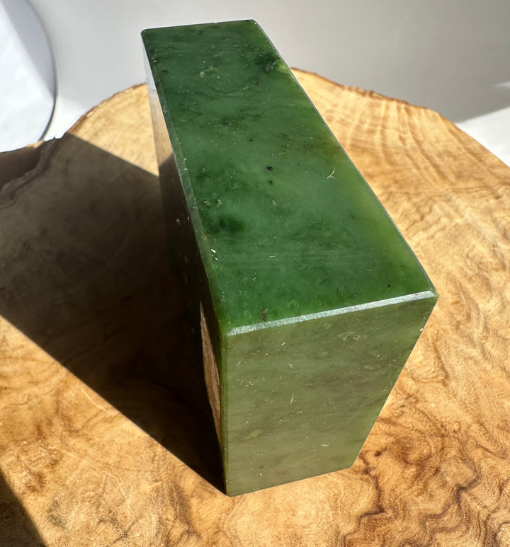 Green jade block viewed from the side on a wooden surface with a rough top edge