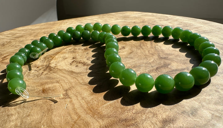 Close up of glossy green 8mm beads on clear thread resting on wood