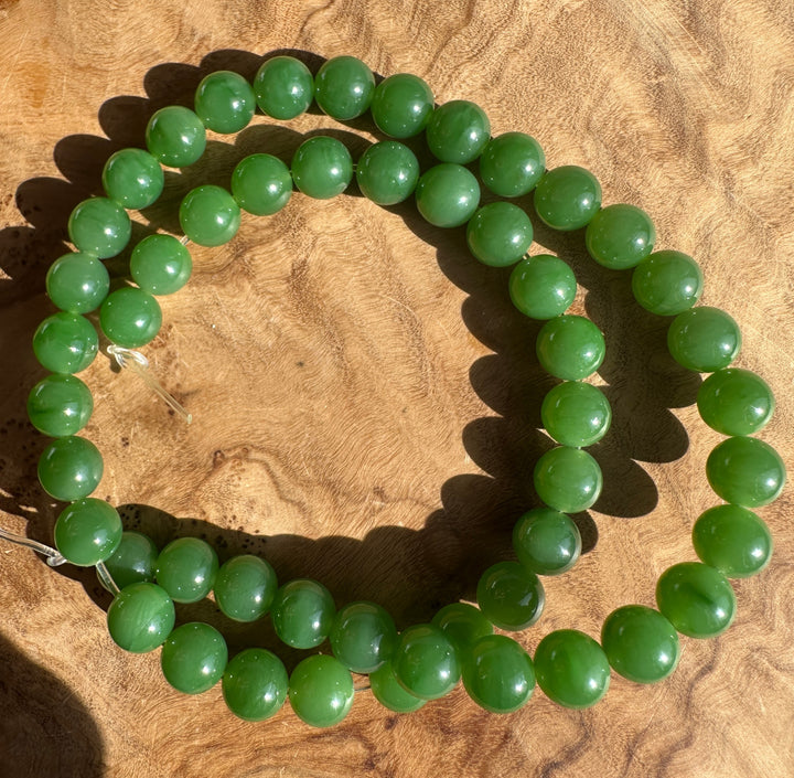 8mm green Siberian jade beads on a clear string laid on tan fabric