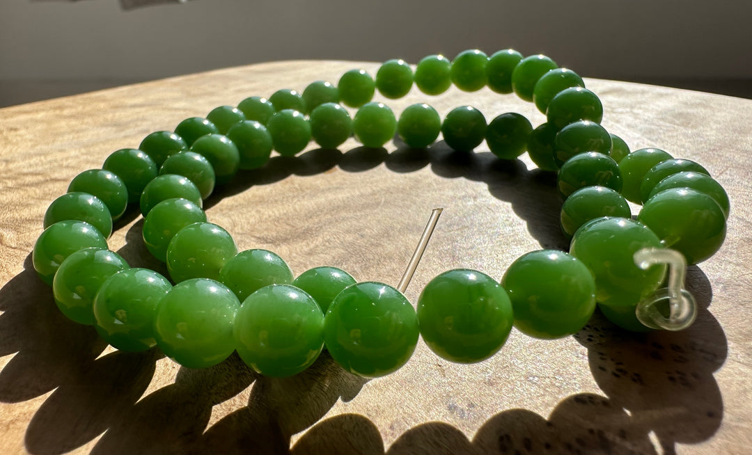 Bright green round beads forming a circular bracelet on a sunlit wooden surface