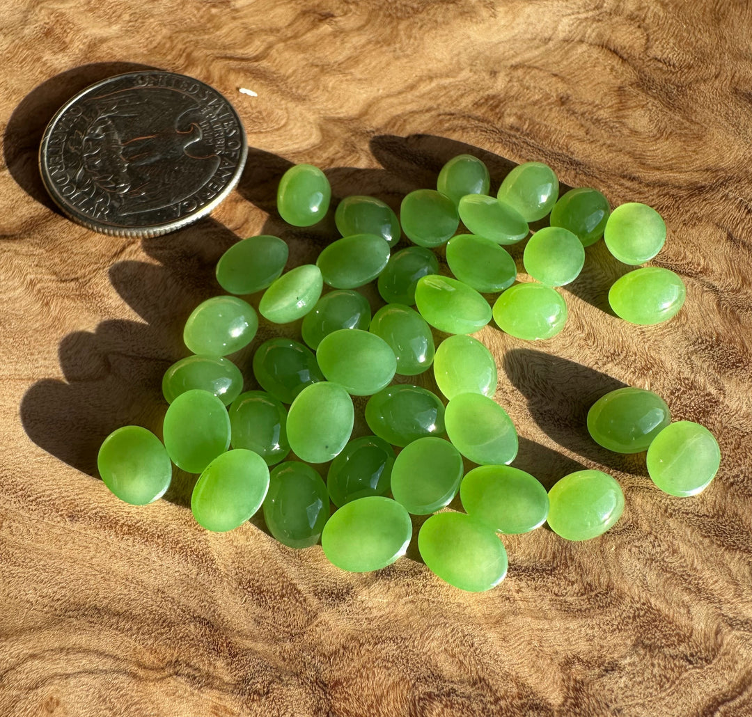 Group of light green oval jade cabochons beside a quarter for scale