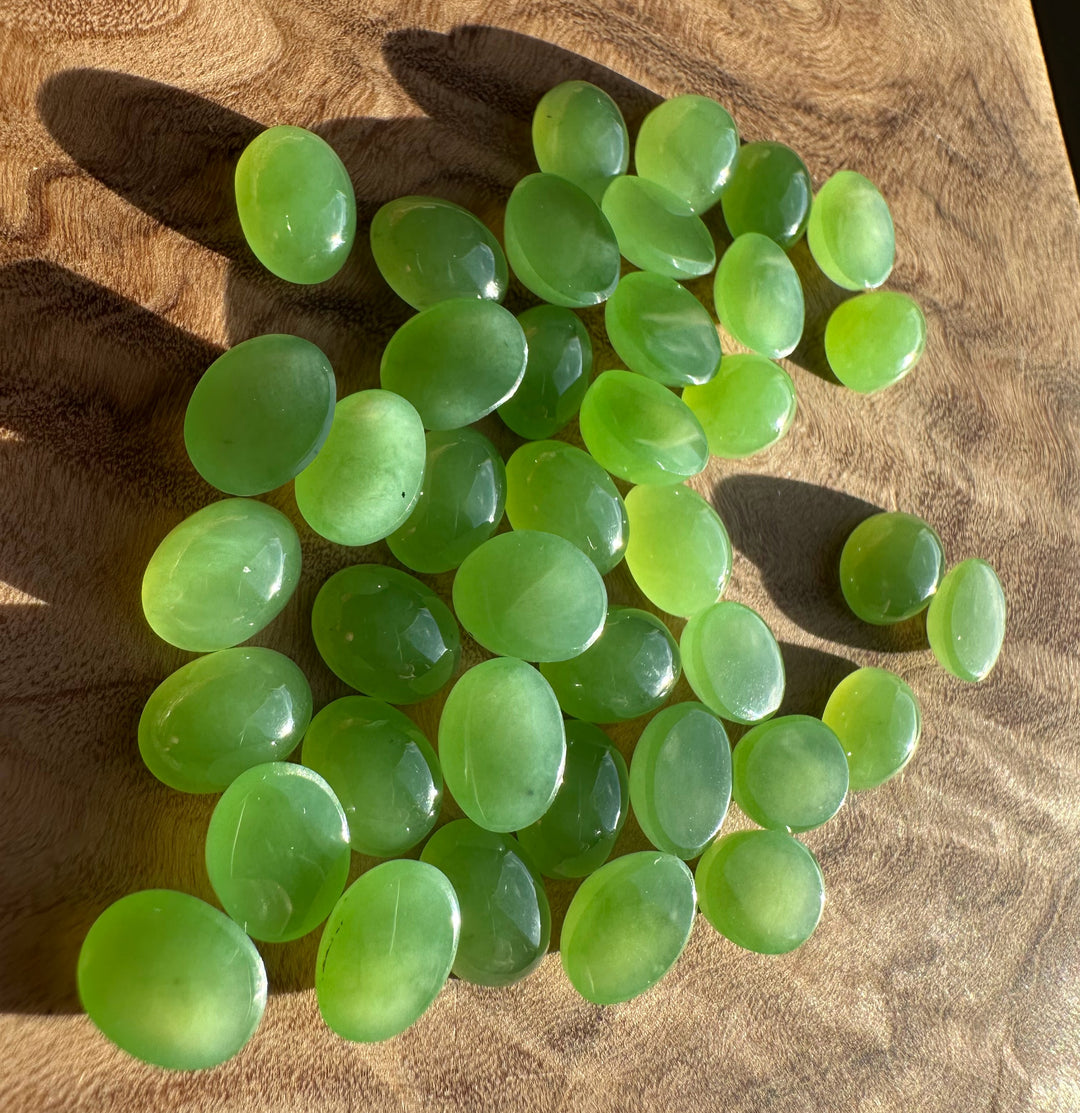 Cluster of AA Siberian oval cabochons 8x6mm bright green on a brown textured surface.