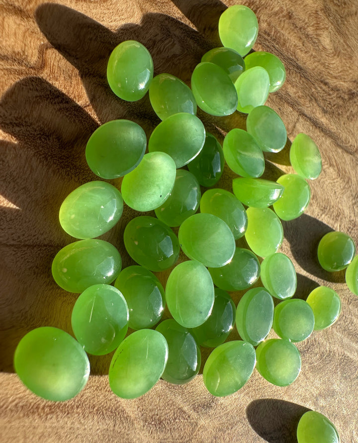 Group of bright green AA Siberian oval cabochons 8x6mm on brown suede background
