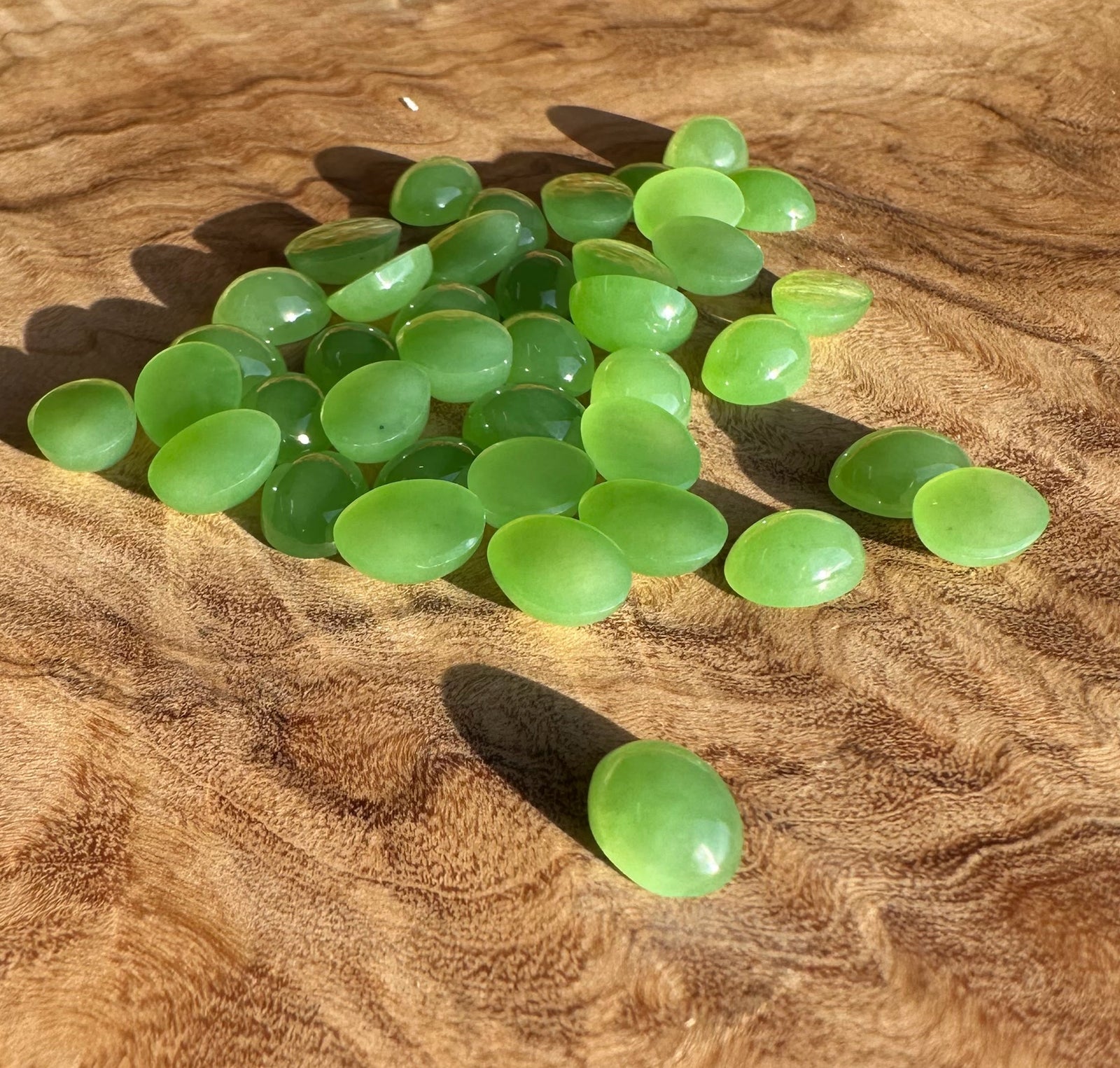 Group of AA Siberian oval cabochons 8x6mm in bright green scattered on brown fabric.
