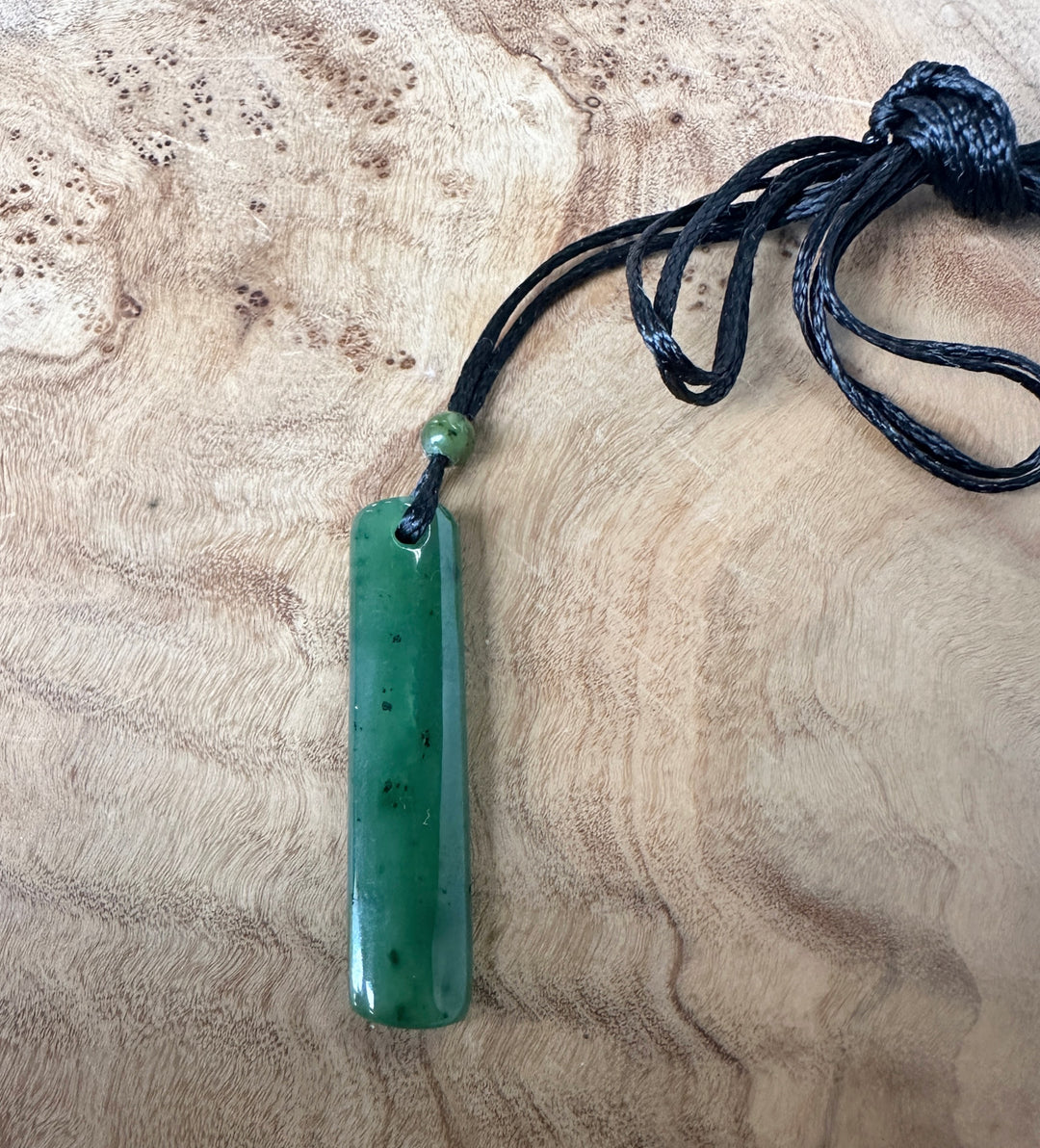 Green jade pendant on a black cord, on a wooden surface