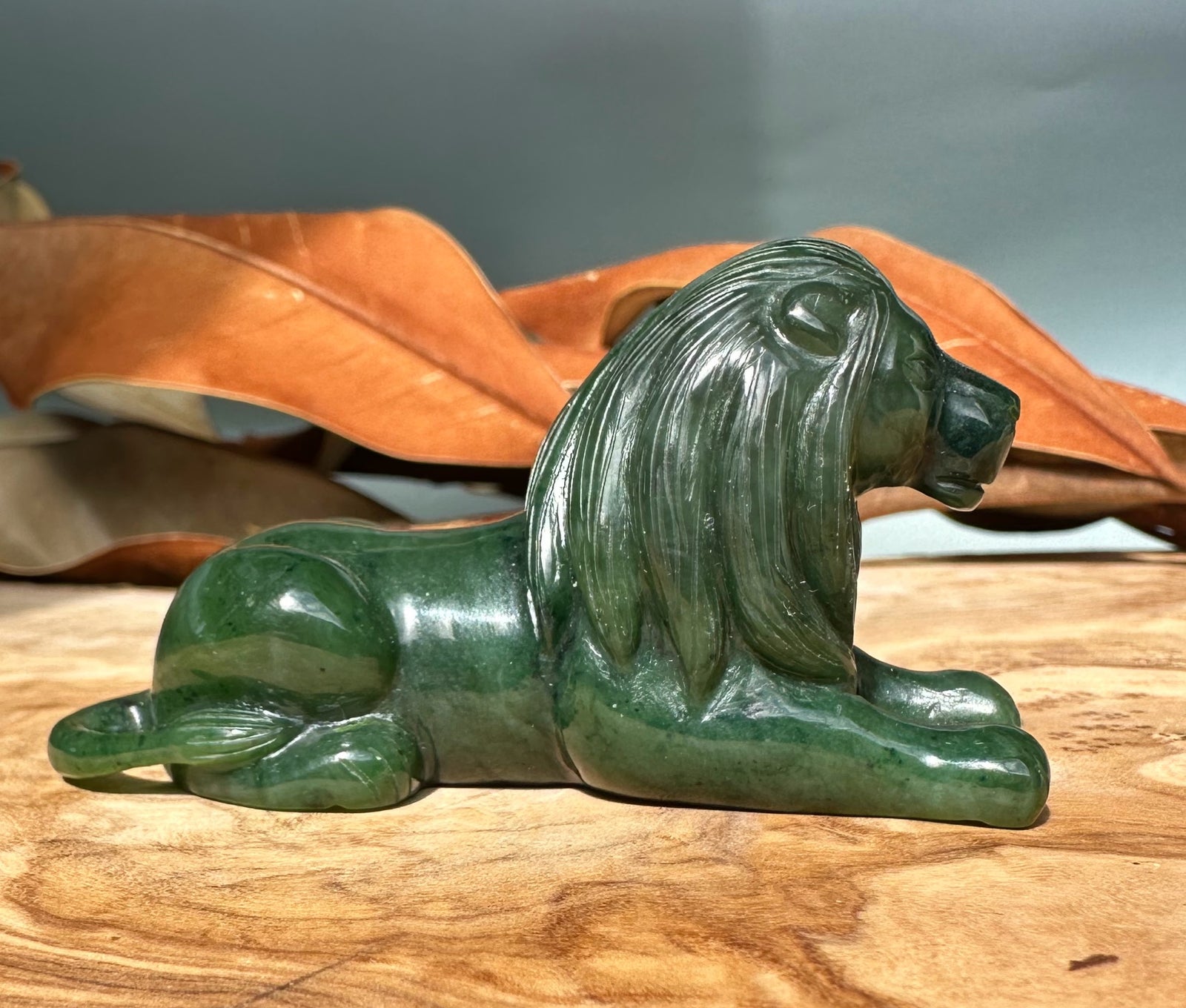 Green Canadian jade lion sculpture carved in a reclining pose with a flowing mane