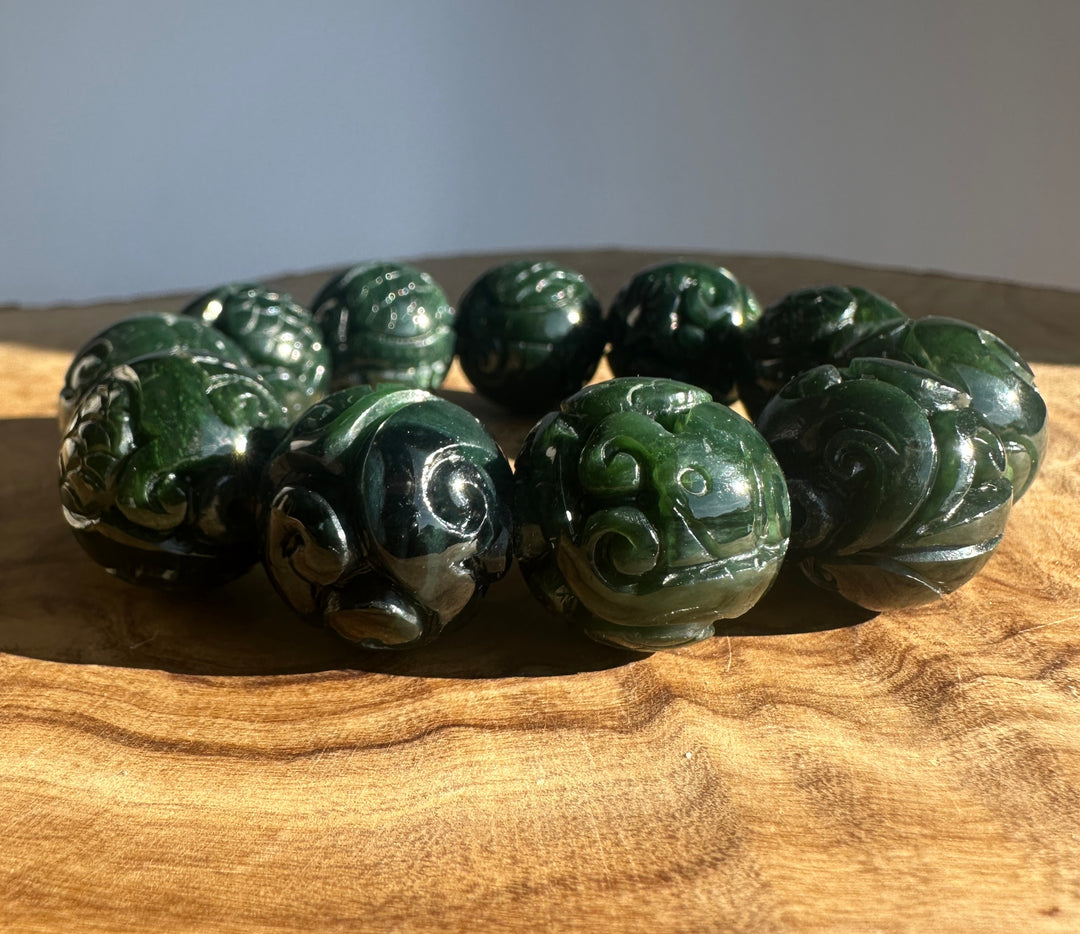 Dark green carved jade bead bracelet with round spiral beads on a wooden surface