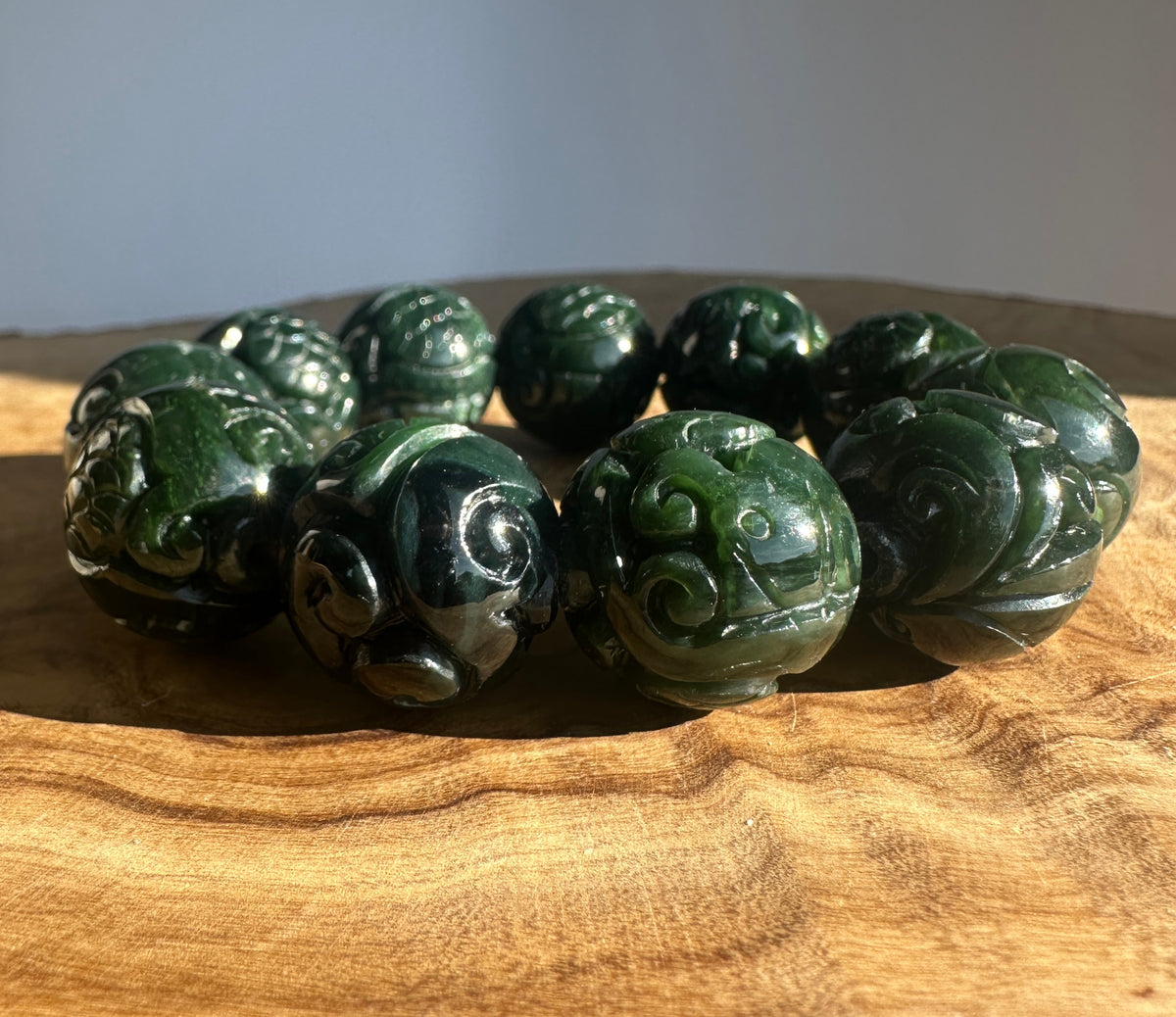 Dark green carved jade bead bracelet with round spiral beads on a wooden surface