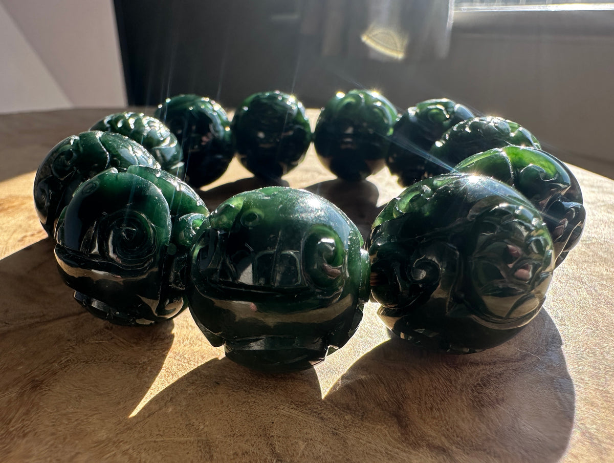 Dark green carved jade bead bracelet displayed on a wooden surface