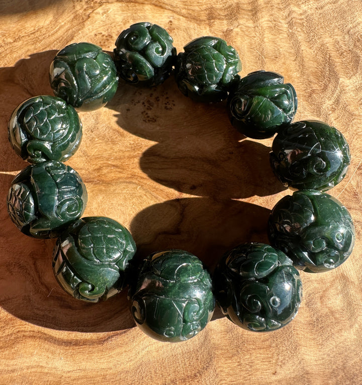 Dark green carved jade bead bracelet with rose shapes on a wooden surface