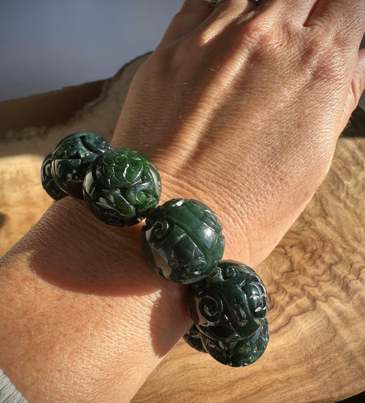 Close up of a dark green carved jade bead bracelet worn on the wrist