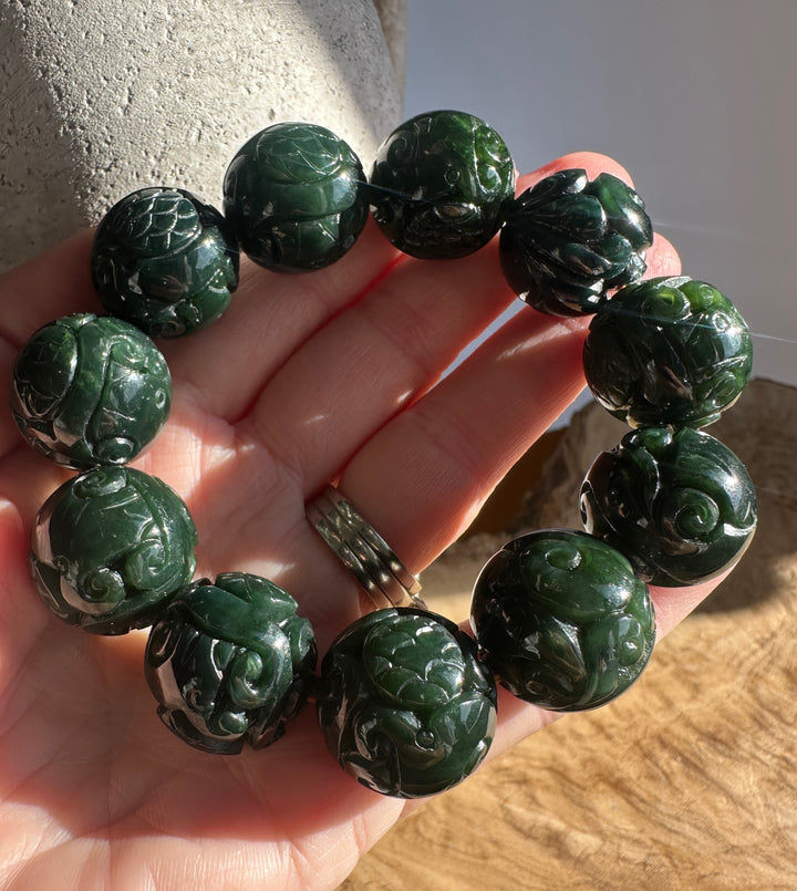 Dark green jade bead bracelet held in the hand showing intricate carvings