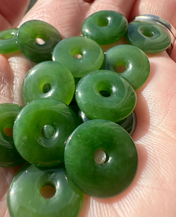 Close up of glossy green jade donut beads with central holes held in a hand