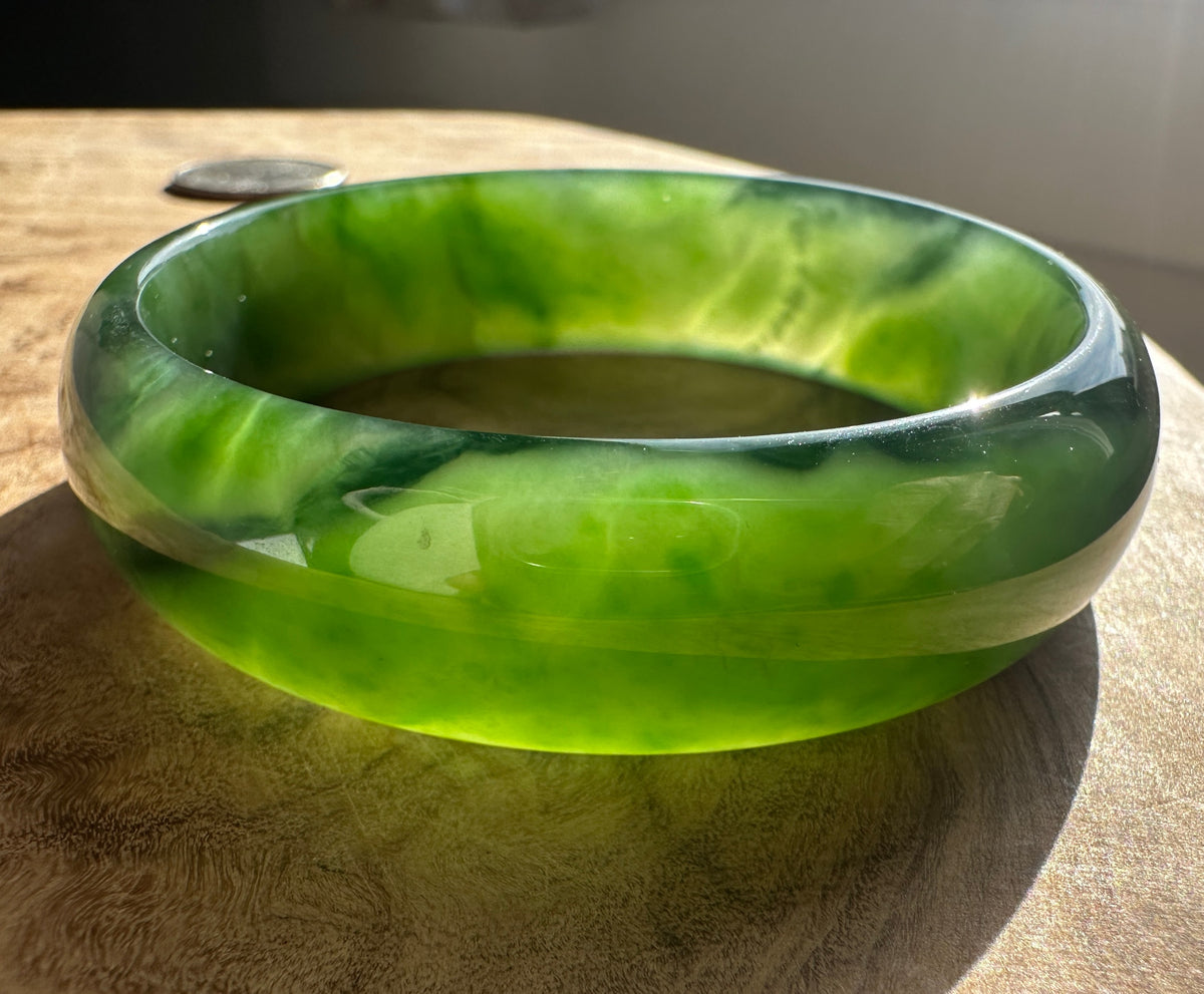 Side view of a green Canadian jade bangle showing interior color and thickness on a wooden surface
