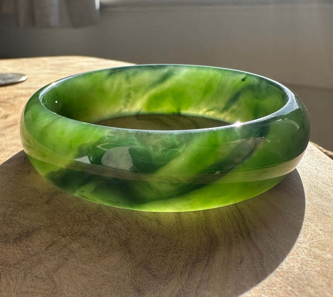 Interior view of a green jade bangle with marbled pattern resting on a wood surface