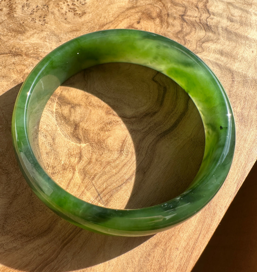 Close-up of a glossy green jade bangle with marbled light and dark swirls on a wood surface