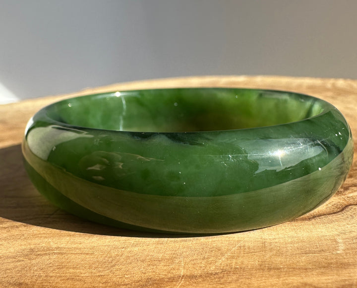 Canadian jade bangle with smooth green surface resting on a wooden table