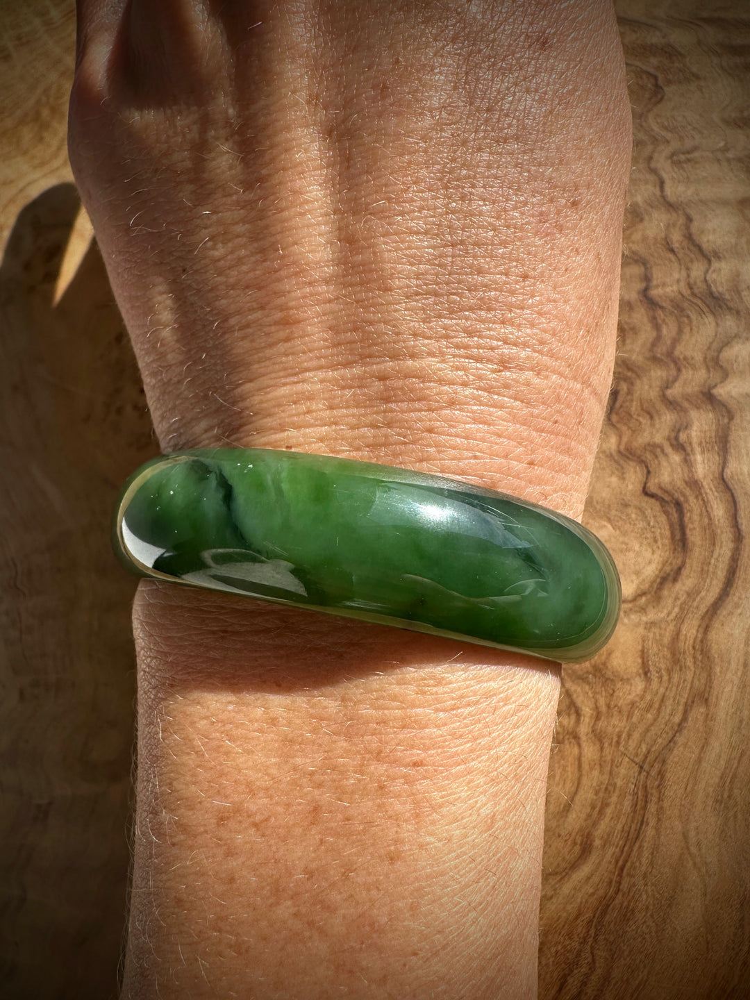 Canadian Jade Bangle worn on the wrist; thick glossy green jade with a slim metallic edge.