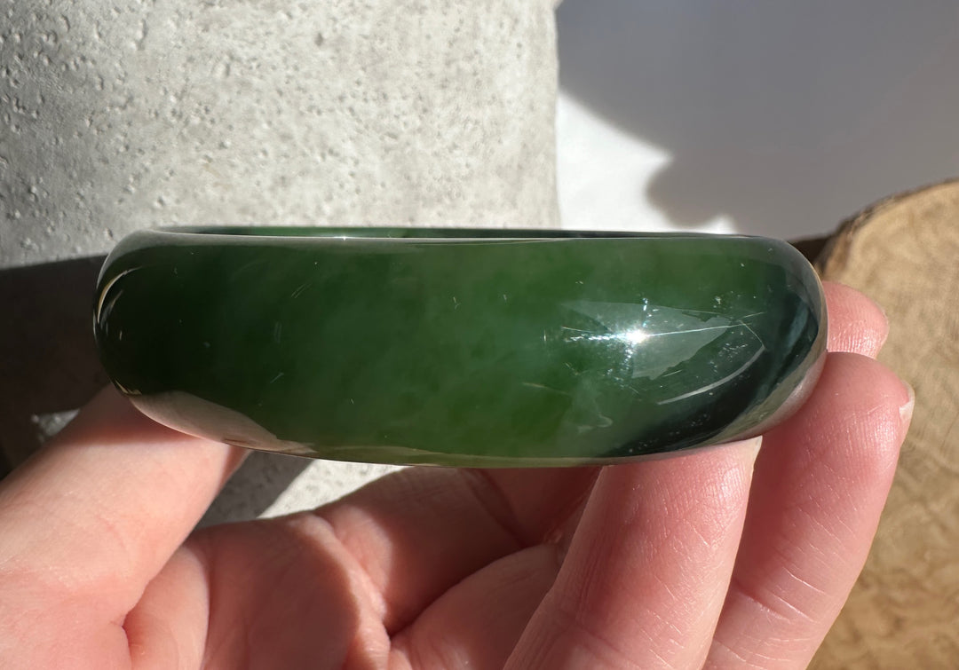 Side view of Canadian Jade Bangle held along the wrist; dark green jade band with a smooth rounded surface.