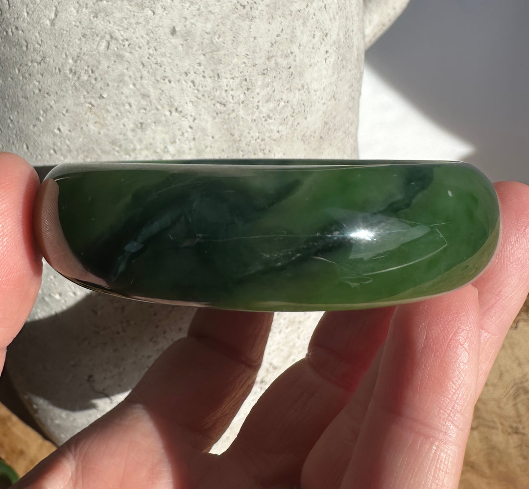 Close up of the jade bangle from the side showing deep green translucence and rounded shape.