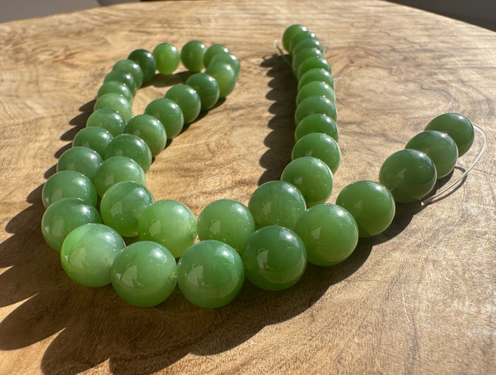Light to medium green 10mm Siberian jade beads arranged in a loose loop on a wooden surface