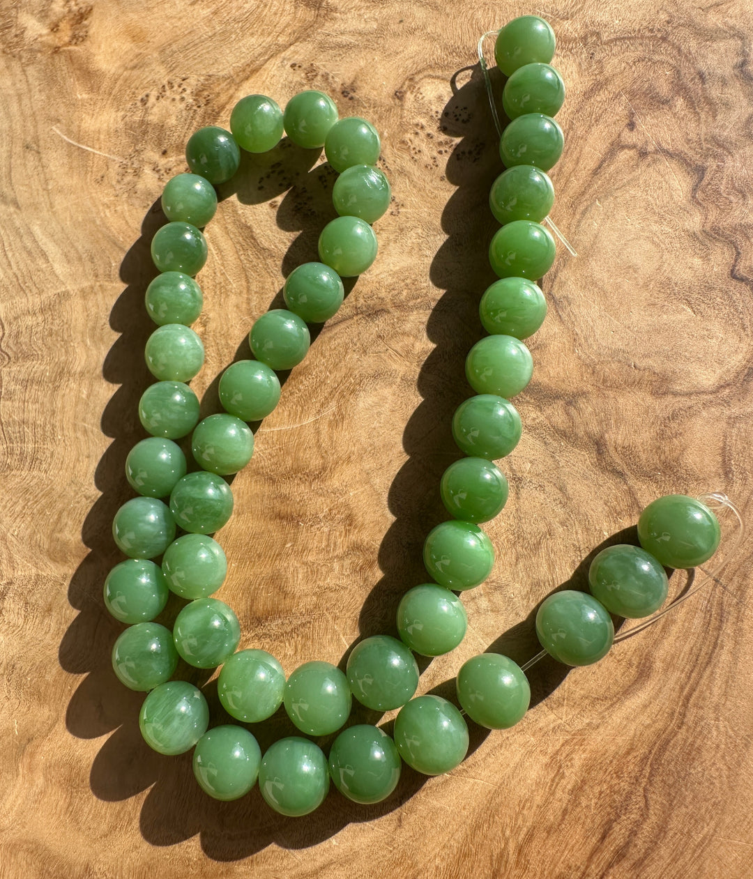 Light green 10mm A+ grade Siberian jade beads arranged on a wooden surface