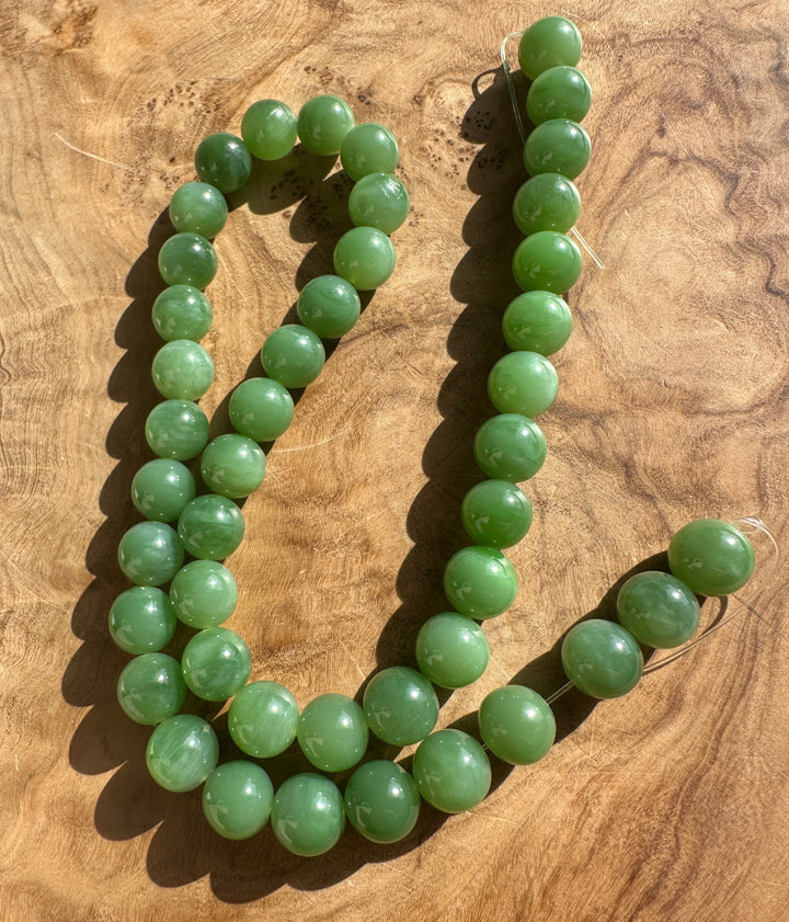 Light green 10mm A+ grade Siberian jade beads arranged on a wooden surface
