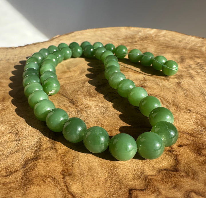 Close up of glossy green 10mm Siberian jade beads held in a hand